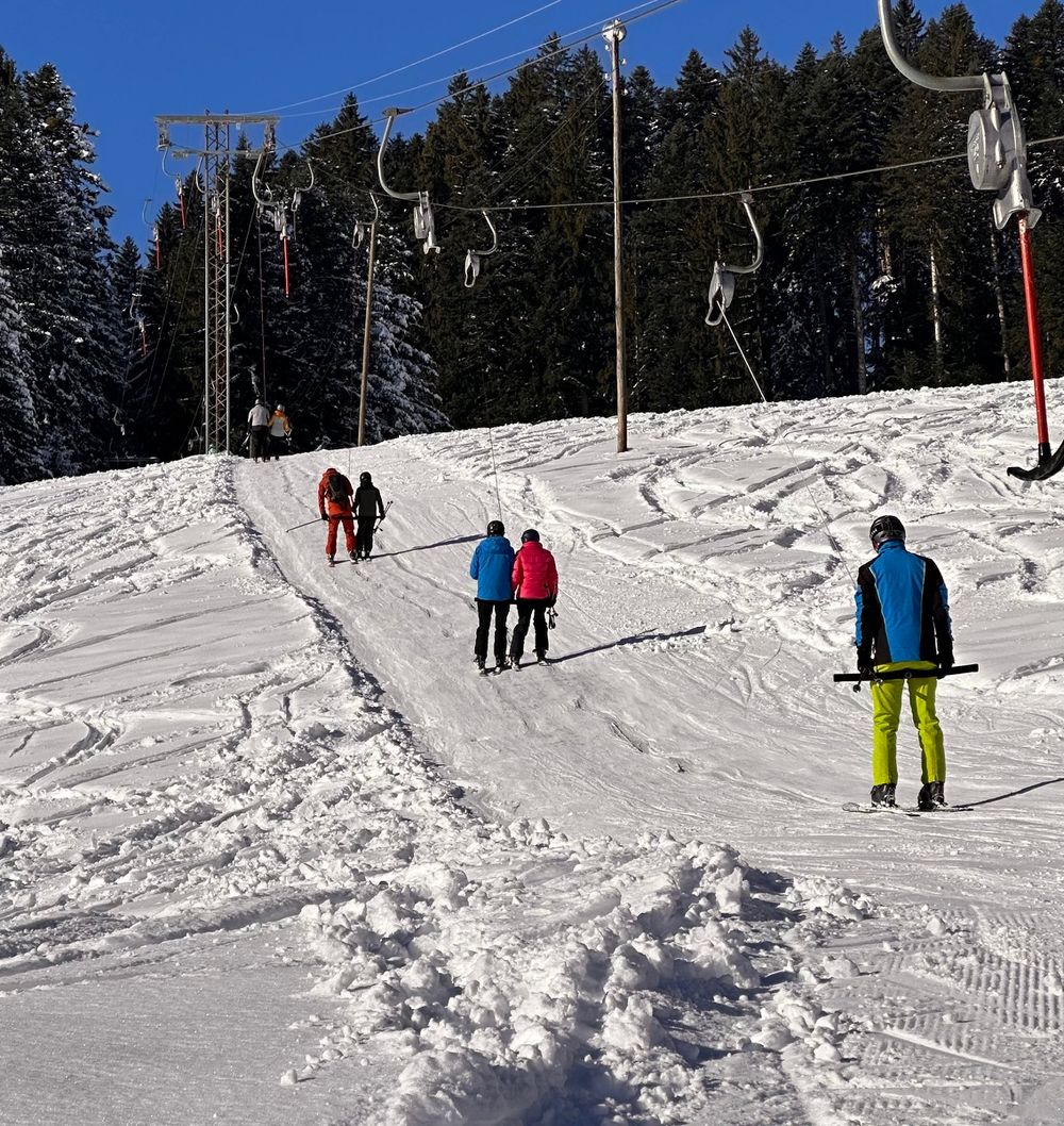 Skifahrerinnen und Skifahrer fahren am Bügellift hinauf, blauer Himmel