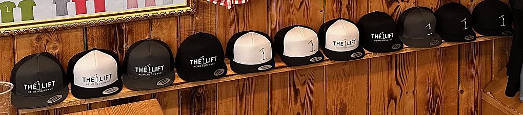 Eine Reihe THE LIFT Caps in Schwarz, Anthrazit und Weiss auf einem Holzbrett