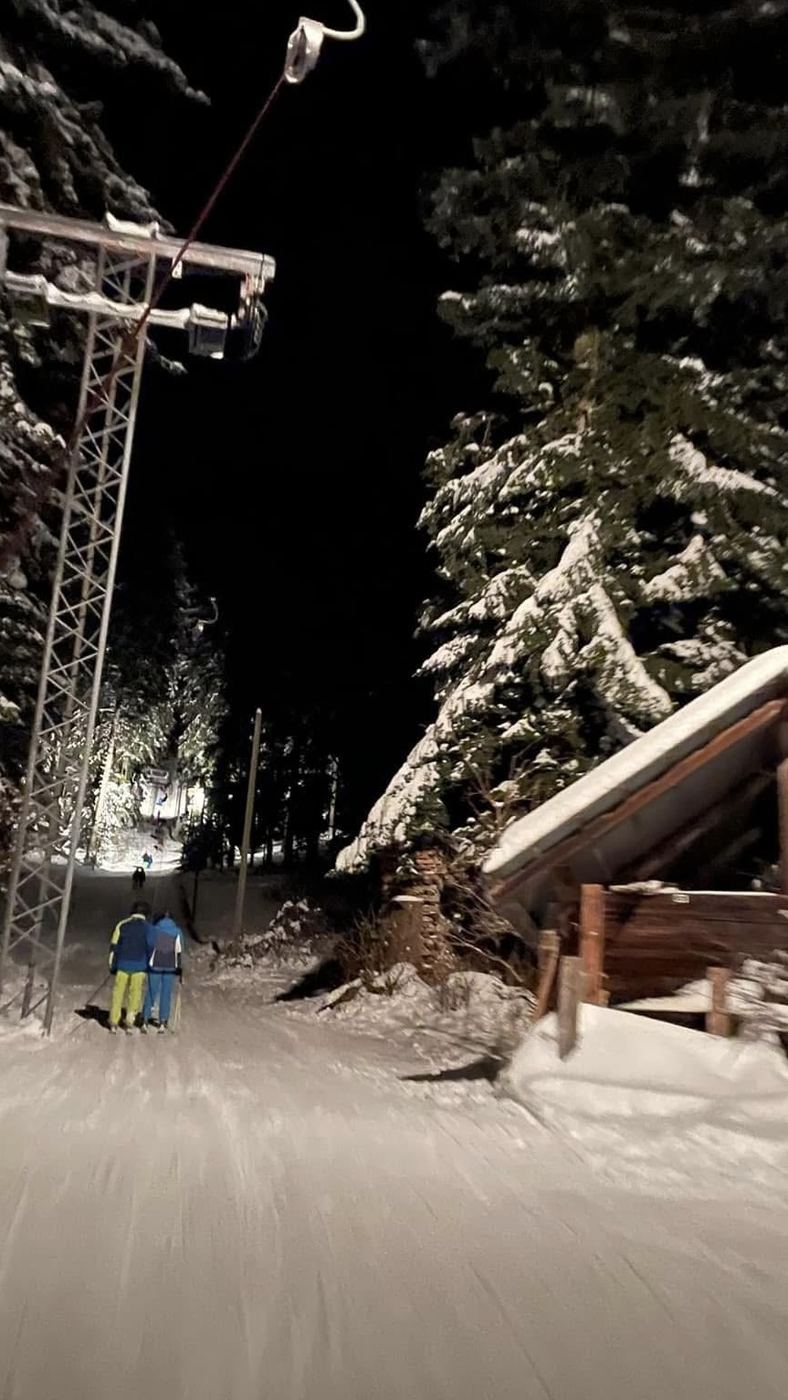 Zwei Skifahrende am Bügel durch den beleuchteten Wald